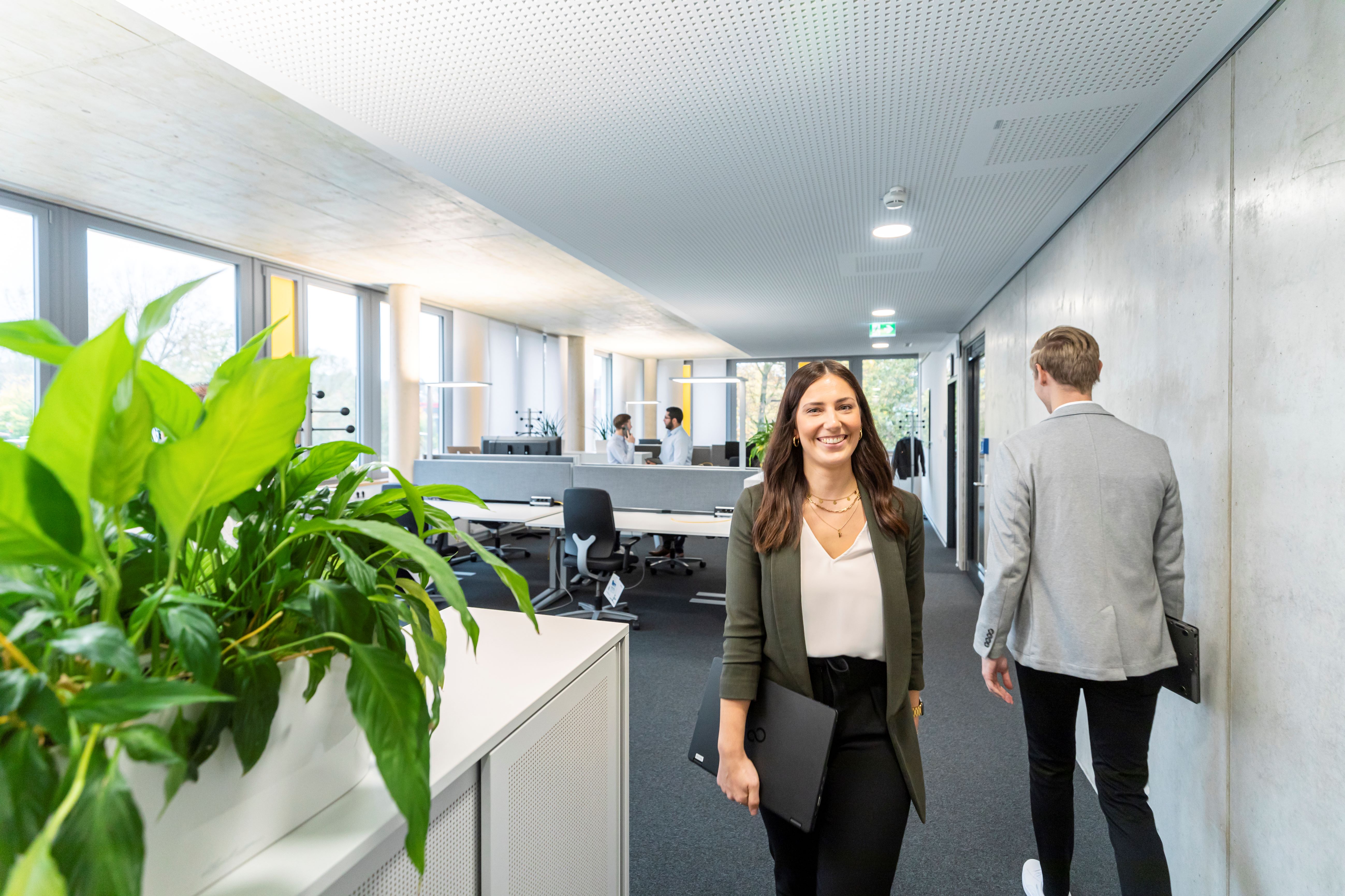 Eine Frau läuft mit einem Laptop in der Hand durchs Büro 